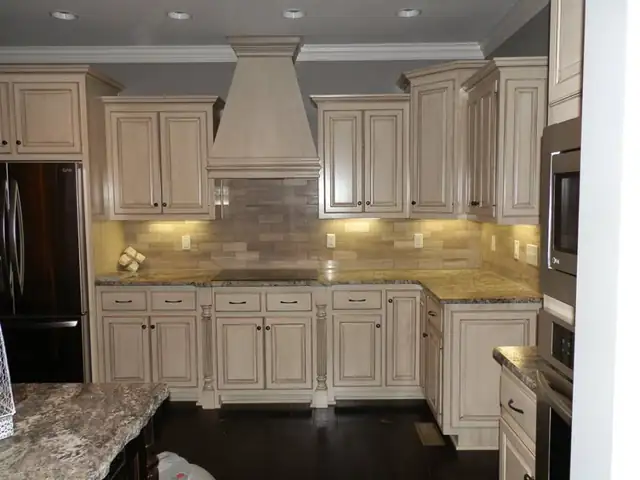 Cream glazed raised-panel cabinets with a tall wood hood, granite counters and under-cabinet lights